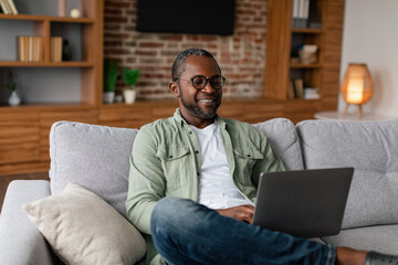 Happy adult african american male in glasses watching video on laptop, study, enjoy rest at free...