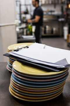 Clipboard on stack of plates on kitchen counter in restaurant