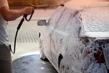 A man washes a car in the summer at a self-service car wash. Applying foam and soap to the car