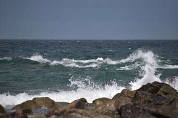 Das Meer ist wellig und bricht wild mit spritzendem Wasser und Gischt an rauen und dunklen Steinen in der französischen Region Bretagne