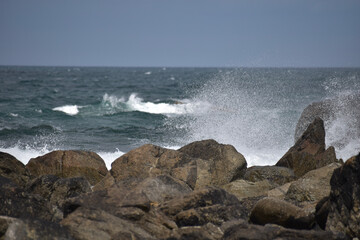 Das Meer ist wellig und bricht wild mit spritzendem Wasser und Gischt an rauen und dunklen Steinen in der französischen Region Bretagne