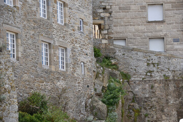 Fototapeta premium Historic stone buildings with multiple windows, situated on a rocky slope, showcasing detailed masonry and a natural environment. The scene exudes a rustic and timeless charm.
