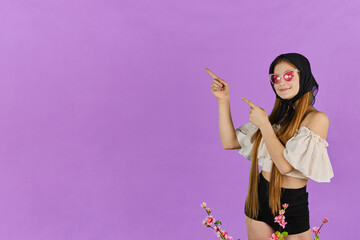 Young long hair woman shows something, point finger left at blue studio background. Girl pointing fingers left and smiling, showing advertisement.