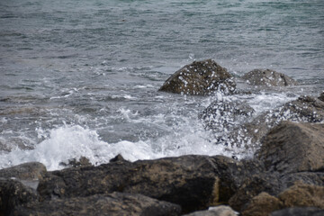 Das Meer ist wellig und bricht wild mit spritzendem Wasser und Gischt an rauen und dunklen Steinen in der französischen Region Bretagne