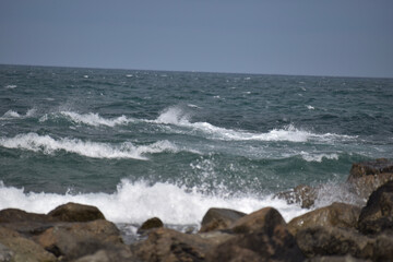 Das Meer ist wellig und bricht wild mit spritzendem Wasser und Gischt an rauen und dunklen Steinen in der französischen Region Bretagne
