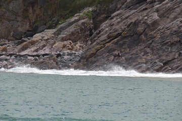 Das Meer ist wellig und bricht wild mit spritzendem Wasser und Gischt an rauen und dunklen Steinen in der französischen Region Bretagne