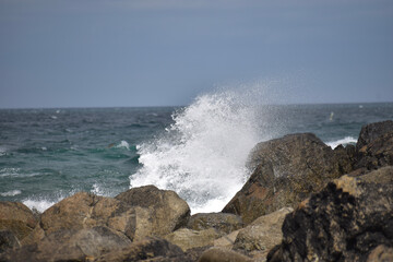 Das Meer ist wellig und bricht wild mit spritzendem Wasser und Gischt an rauen und dunklen Steinen in der französischen Region Bretagne