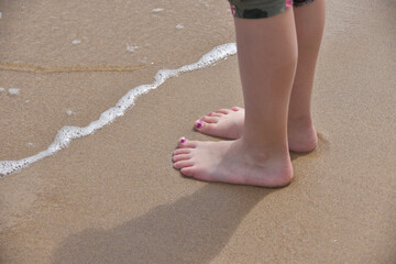 Füße in Sandalen und Barfuß ohne Socken am Strand auf einem Pfad mit Sand und Meer Wasser