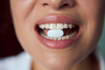 Selective focus on a white pill with vitamins, minerals and dietary supplement in the mouth of blurry happy pregnant woman, smiling beautiful toothy smile. Pregnancy care concept. Prenatal health