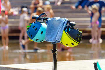 Protective helmets and pants hang on the handlebars of a scooter children bathe in a fountain