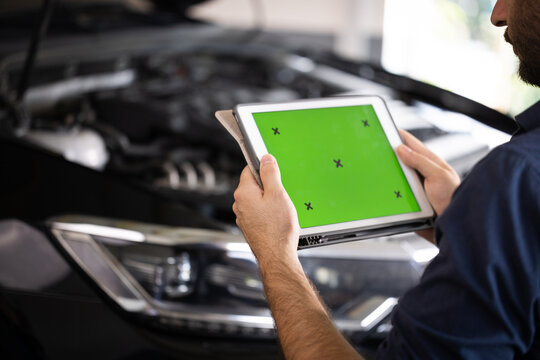 Mechanic running diagnostics software on tablet computer with green screen mockup chromakey. Unrecognizable vehicle service manager worker check and maintenance to repair the engine car in workshop