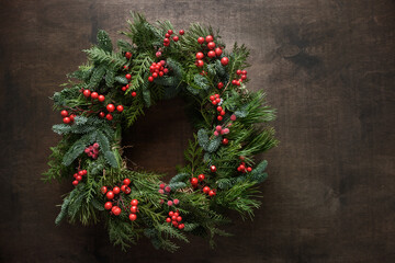 Christmas wreath of natural evergreen branches with red holly berries on brown background....