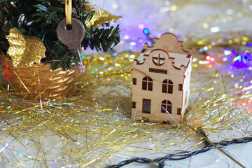 Miniature wooden house with a key on a Christmas tree. New year gift, present on a golden tinsel. Mortgage, home, real estate, realtor concept. On white background