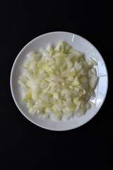 Juicy onion in a white plate on a black background. Delicious sliced onion in a bowl.