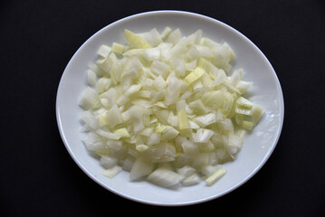 Juicy onion in a white plate on a black background. Delicious sliced onion in a bowl.