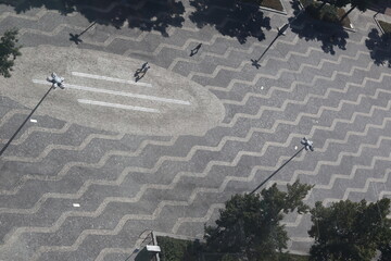 City square from above with grey zigzag pattern and shadows from lampposts, trees and walking...