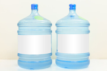 Two plastic gallon water bottle containers with white labels stand on a blue background. Water...