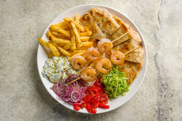 souvlaki with shrimp kebab, french fries, vegetables and pita top view on stone table