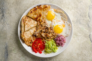 Greek Breakfast on a plate with two eggs, pita, vegetables top view on stone table
