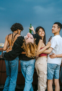 Portrait of young man bending backwards while standing amidst friends on rooftop