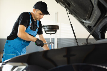 Empowering male mechanic is working in car service. Man is working on an usual car maintenance....