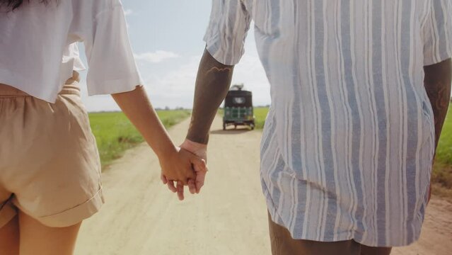 Rear view of young couple holding hands while walking on dirt road