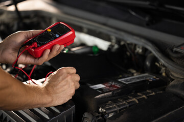 Check battery voltage with electric multimeter. Man using multimeter to measure the voltage of the batteries. Mechanic doing car inspection, he is testing car battery with tester - obrazy, fototapety, plakaty