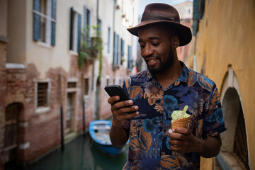 A tourist in Venice uses his smartphone while eating an ice cream, concept of technology on...