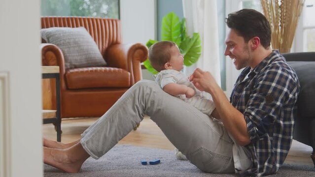 Loving Transgender Father Playing Peek-A-Boo With Baby Son Sitting On Floor At Home