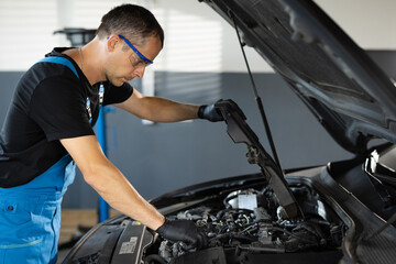 Fototapeta na wymiar Mechanic man open a car hood and check up the engine. Car mechanic noting repair parts during open car hood engine repair at garage. Overheating of a car engine. Motor with open hood