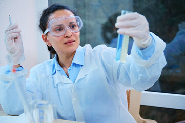 Portrait of a Latin American woman, clinical researcher, scientist pharmacologist holding test tubes with liquid substance, working on new vaccine, making scientific investigations in medical field