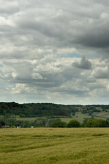 Rolling countryside with a church and some houses under a cloudy sky.