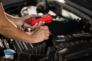 Check battery voltage with electric multimeter. Car starter battery. Professional mechanic is...
