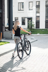 Obraz na płótnie Canvas Back view of sporty woman walking with bike at urban area