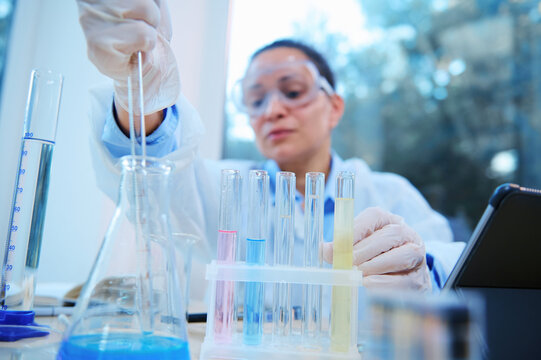 Focus on test tubes with going on chemical reaction on blurred background of a female scientist, lab assistant pipetting liquid substance into flat bottomed flask in scientific research laboratory