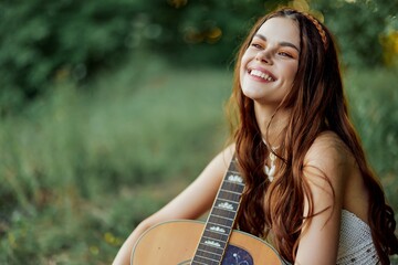Hippie woman smiling and hugging her guitar in nature in the park in the sunset light