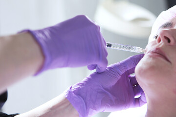 Beautician's hands in gloves close-up. Cosmetic procedures. Injection of a filler for the face....