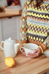 Girl pours hot tea into a cup from a teapot. Enjoy the comforts of home. White cup close-up in the hands of a woman in the rays of the sun from the window. A cup of tea in the hands of a woman
