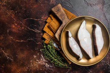 Sliced halibut fish, raw steaks on plate with thyme. Dark background. Top view. Copy space