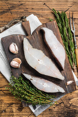 Atlantic halibut fish, raw steaks on wooden board with herbs. Wooden background. Top view