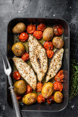 Roasted halibut fish steaks with tomato and potato. Black background. Top view