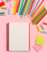 Cuaderno en blanco, boli, post it, bloc, clips, lapices y accesorios sobre un fondo rosa pastel liso. Vista superior y de cerca. Copy space. Formato vertical