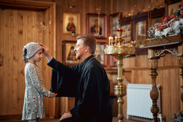 a priest blesses a little girl in a headscarf in an Orthodox church after a festive church mass