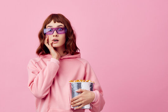 Cool movie. Confused cute redhead lady in pink hoodie sunglasses with popcorn posing isolated on over pink studio background show copy space Banner. Fashion Cinema concept. Entertainment offer