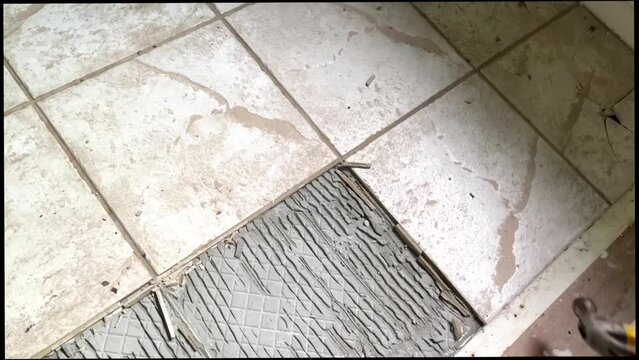 An unrecognizable man removes tiles from the floor with a hammer and tools. Repair work. High quality FullHD footage