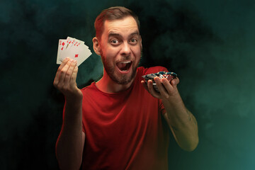 Studio portrait of excited man posing with a stack of playing cards and a pile of poker chips in...