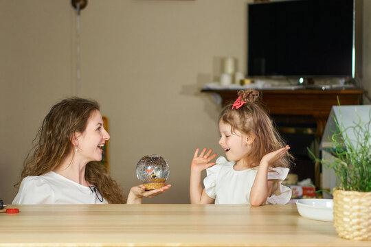 Magic Surprise for child. Snow globe as gift. Happy childhood. Woman surprised little beautiful girl in white. Happy childhood. Have fun together. Give gift to children. Mom congratulated her daughter - Powered by Adobe