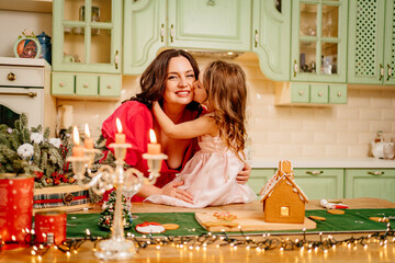 a little girl in a chef's cap with mom makes a gingerbread house