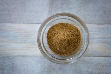 Bowl of grated coriander on gray wooden background, top view