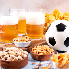 Beer in glasses and snack on wooden table with football ball, football game night food